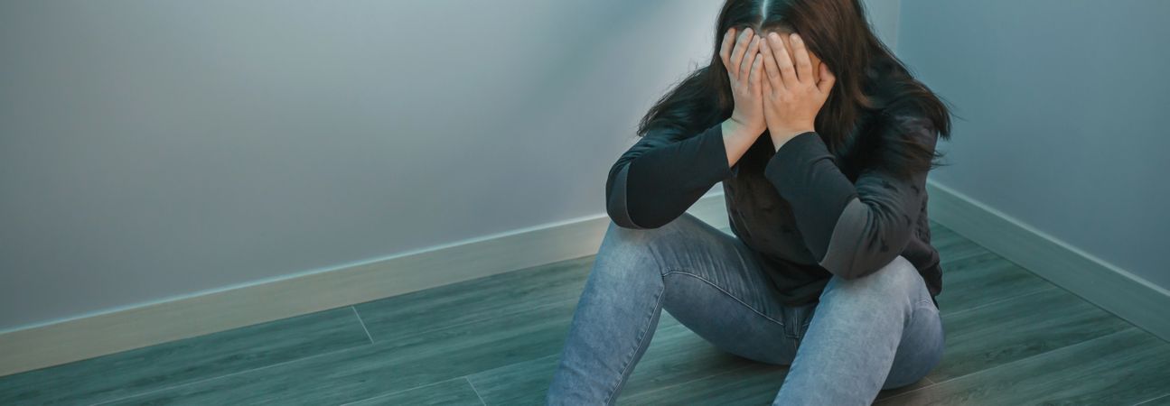Depressed woman with hands in face sitting on the floor