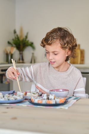 Preteen boy eating sushi with chopsticks