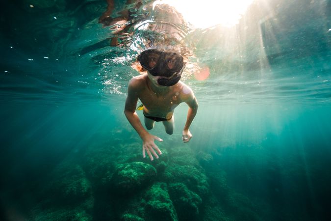 Young guy in snorkeling goggles swimming underwater of sea