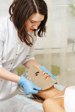 Female beautician placing mask on woman’s face during facial