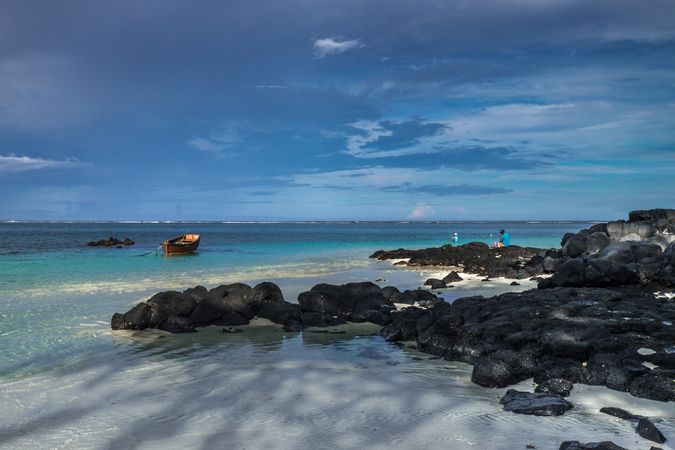 People on lava rocks looking out at red fishing boats