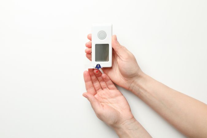 Female checking blood sugar level on blank background