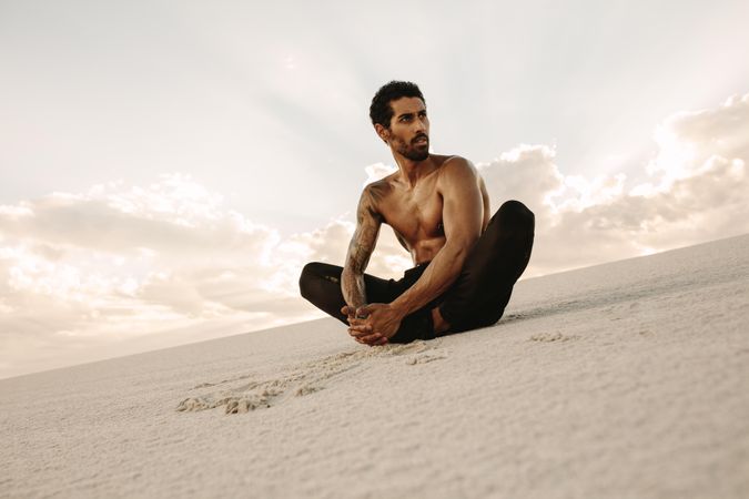 Runner sitting in desert with feet joined together and looking away