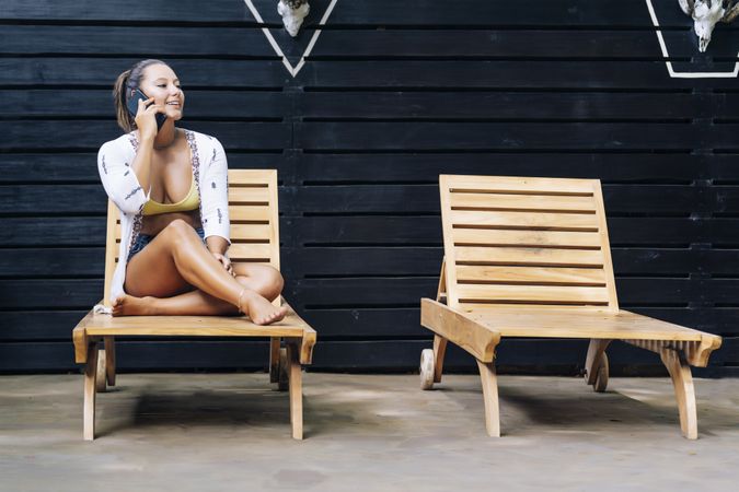 Delighted woman talking on phone while resting on deck chair