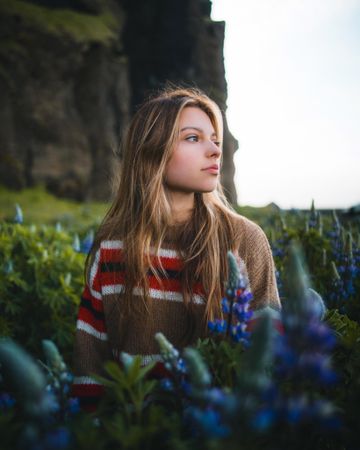 Portrait of young woman in brown and red sweater sitting in blue flower field