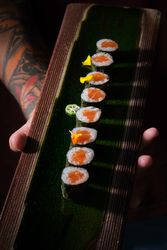 Crop waiter showing sushi rolls on wooden tray