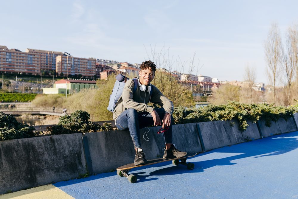 Young cheerful Black male sitting with skateboard