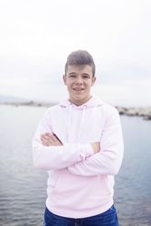 Young male teenager with crossing arms standing on promenade while looking at camera, vertical