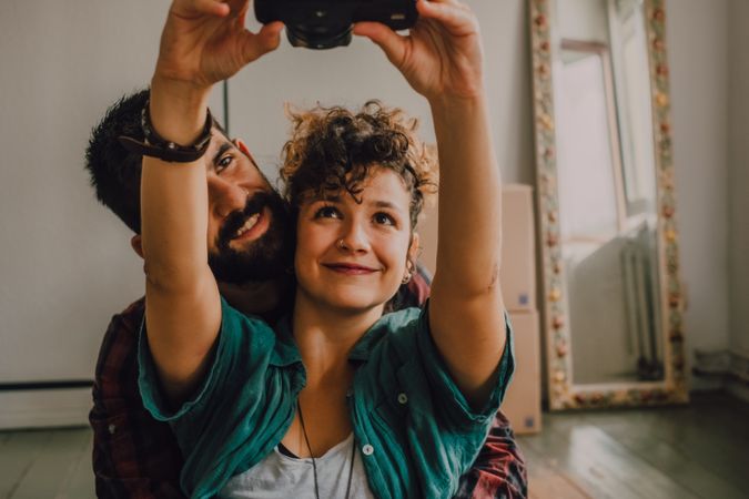 Joyful couple embracing and taking selfie on camera at home