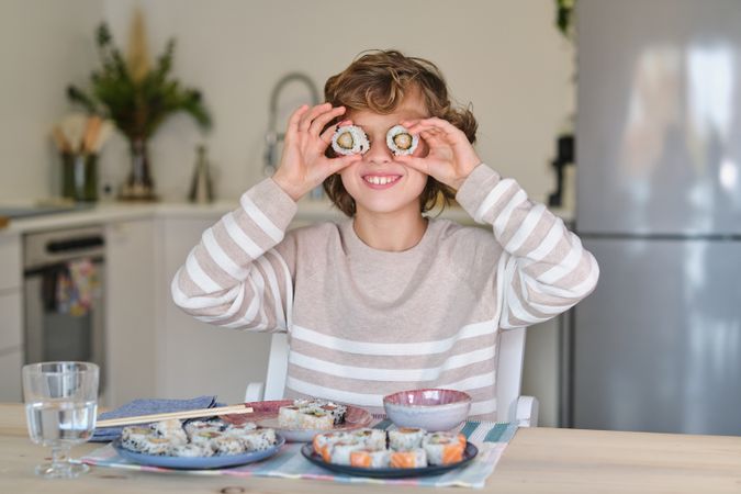 Glad kid putting sushi rolls on eyes at table