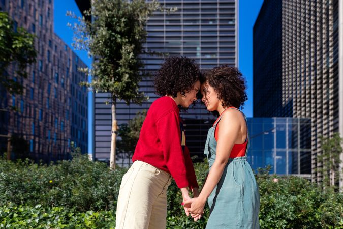Female couple holding hands and facing each other in city park with office buildings in background