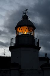 Shining lighthouse against cloudy sky