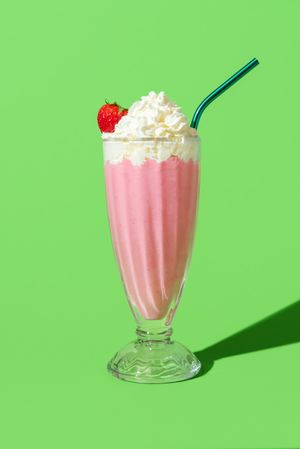 Strawberry milkshake with whipped cream, minimalist on a green background