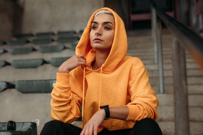 Close up of a fitness woman sitting in the stands of a stadium wearing a hooded sweatshirt