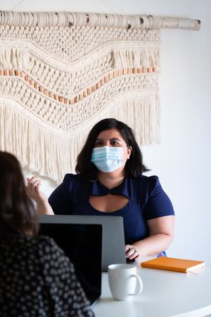 Woman wearing a face mask talking with her colleague in a bright modern office