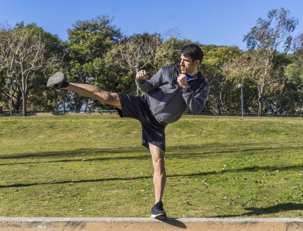 Young athletic martial arts fighter practicing kicks in a public park.