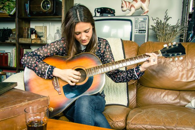 Young hipster woman playing acoustic guitar at home