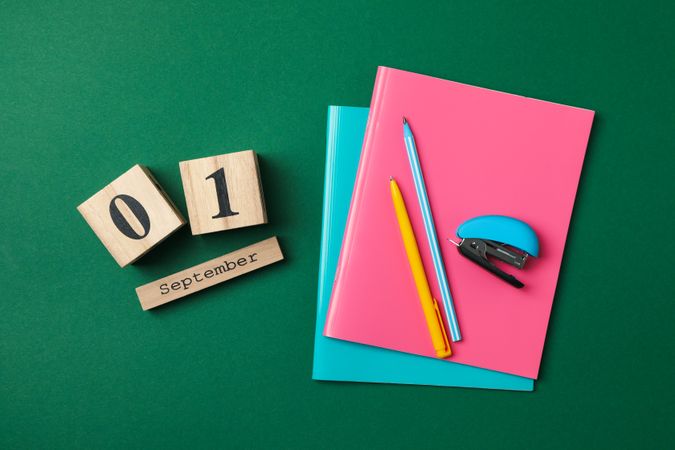 Wooden calendar with 1 september and school supplies on green background