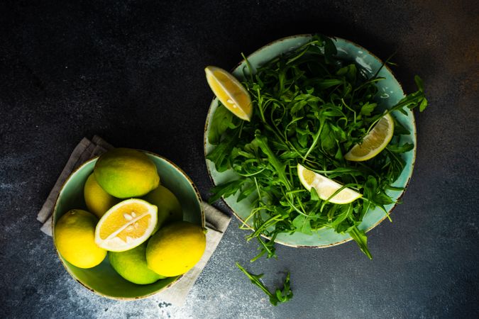 Top view of fresh arugula salad with next to bowl of lemons