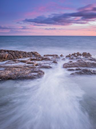Sea waving near rough rocks during sunset