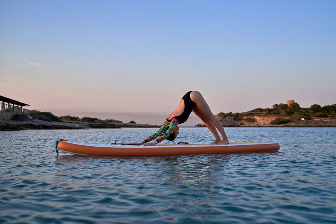 Young woman taking Adho Mukha Shvanasana pose on paddleboard