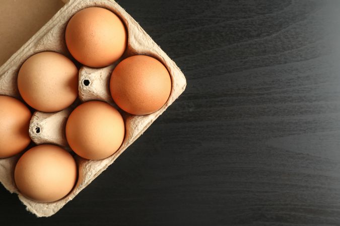 Chicken eggs in carton box on dark background, space for text