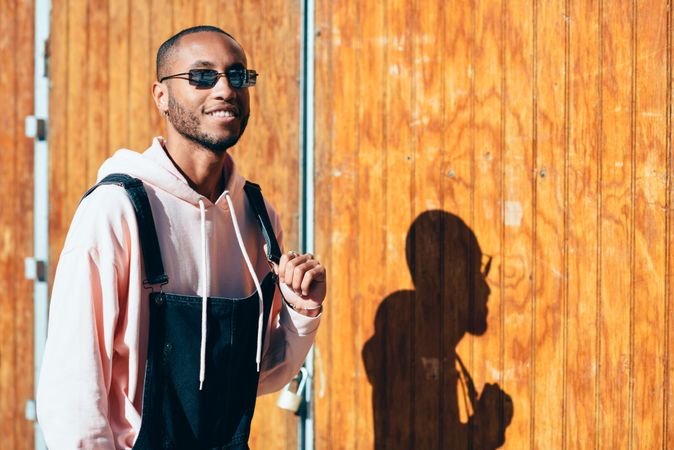 Male wearing overalls and smiling standing by a wooden wall
