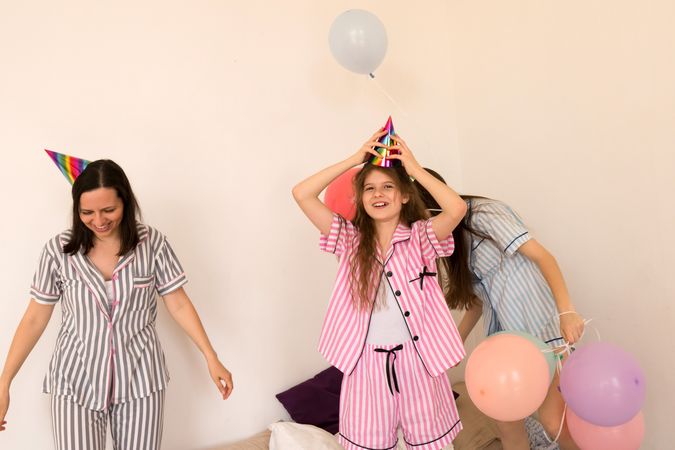 Mother and daughters celebrating with party hats and balloons.