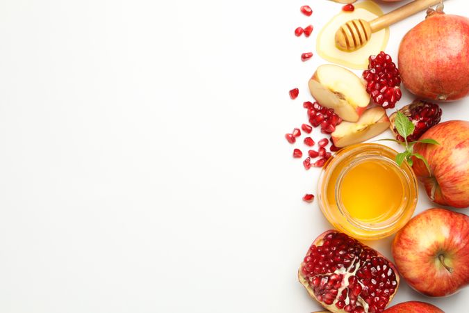 Honey pot, apples, and pomegranate seed arranged on side of picture with copy space