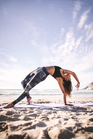 Flexible yoga instructor doing side plank pose on the beach