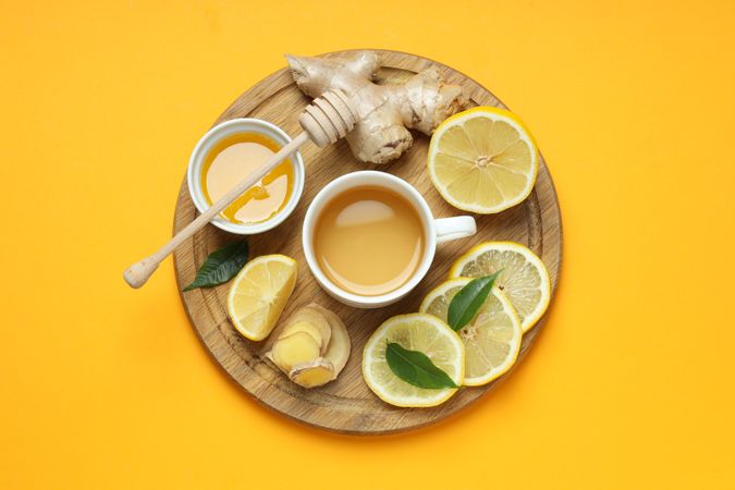 Cup with tea, lemon, ginger and honey on yellow background, top view