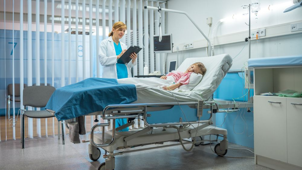 Sick Little Girl Lies on a Bed In the Hospital, Friendly Doctor Writes Medical Record
