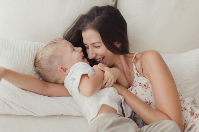 Mother ticking little son and laughing on bed