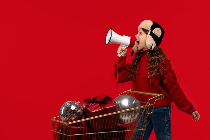 Excited girl in red sweater and hat shouts into megaphone