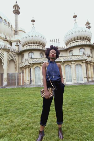 Woman in blue tank top and dark pants standing beside a building