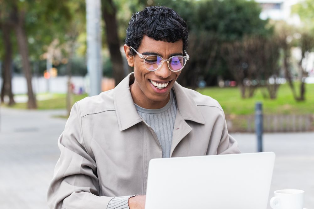 Happy hispanic male freelancer working on laptop in city