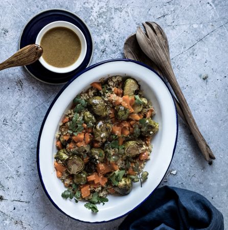 Braised brussels sprouts and pumpkin with quinoa in bowl near cup of sauce
