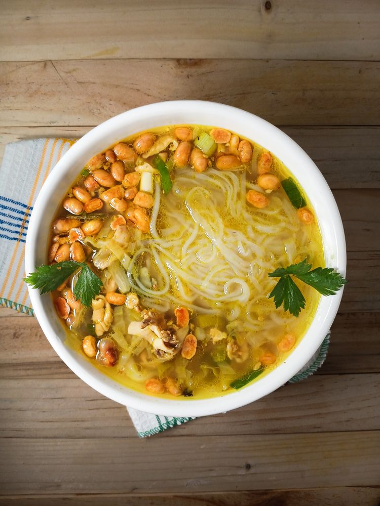 A bowl of yellow soto with noodles, fried soybeans, and celery leaves