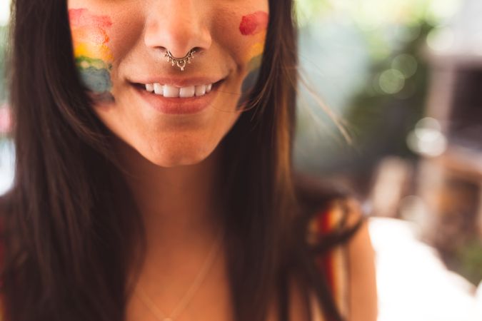 Brunette woman with LGBTQIA symbol on face straightening hair
