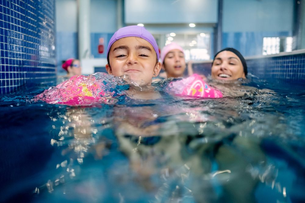 Cheerful girl in hat smiling and swimming in pool in water park