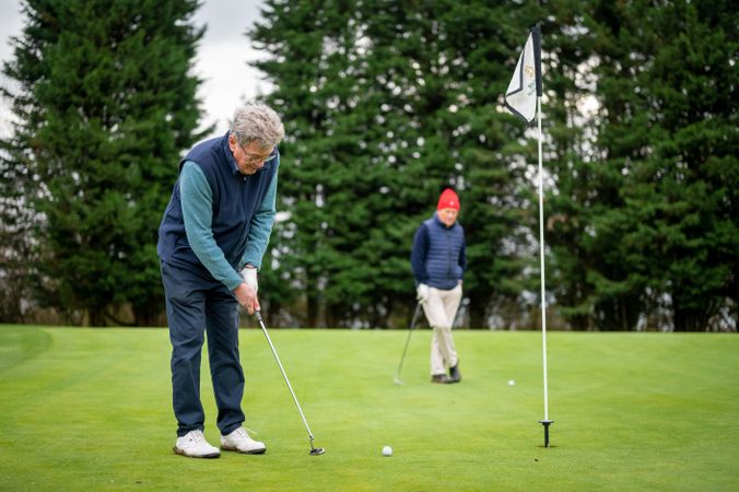 Mature male putting on golf course with friend looking on