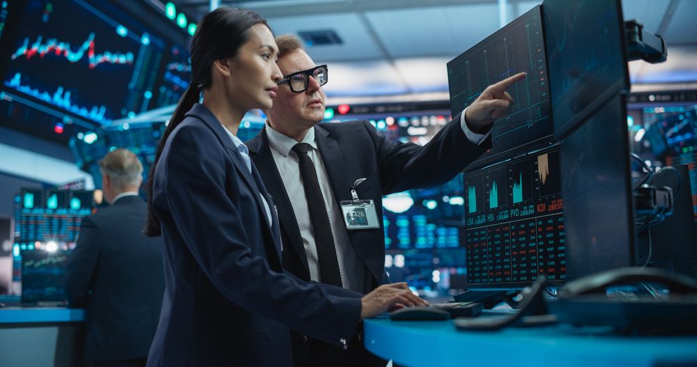 Financial Analysts Using a Computer with Multi-Monitor Workstation with Real-Time Graphs, Financial Reports and Market Charts.