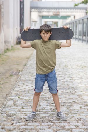 A teenage boy carrying skateboard behind head