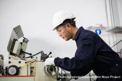 Asian male in hard hat and coveralls operating machine in factory 4mzz7b