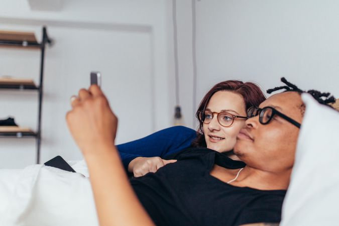 Young man and woman in bed looking at smart phone