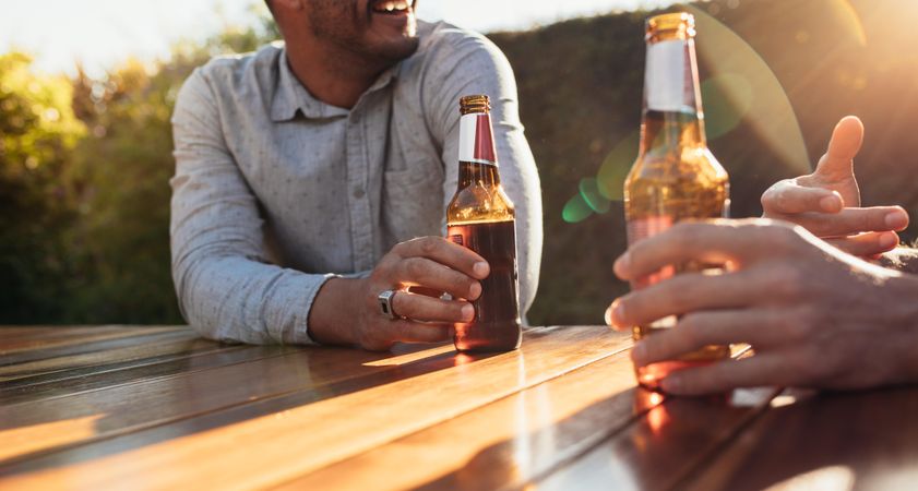 Couple sitting outdoors at wooden table having beers and talking