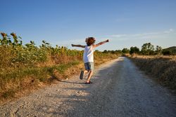 Unrecognizable boy running along endless road in countryside