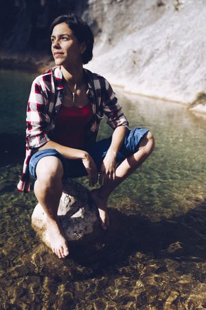 Cheerful woman sitting on rock in clear water
