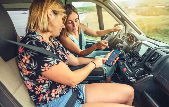 Side view of woman driving a motorhome checking map on phone with friend