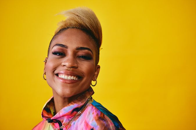 Studio shot of confident smiling Black woman in bold 80s windbreaker jacket and wearing gold jewelry